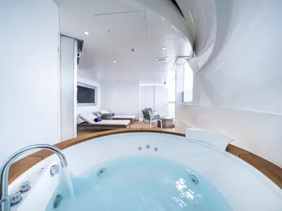 Luxuriöse Owner's Suite an Bord der MSC Seashore mit privatem Whirlpool im Vordergrund. Dahinter ein möbliertes Sonnendeck mit Liegen und Sitzgelegenheiten, beleuchtet von hellem Tageslicht.