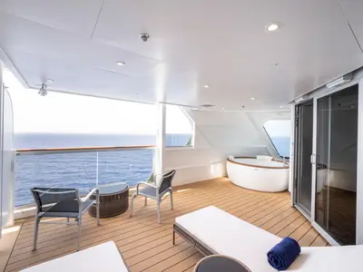 Weitläufiger Privatbalkon der Owners Suite an Bord der MSC Seashore mit Jacuzzi, Sonnenliege und Sitzgruppe aus Rattan. Einladende Terrasse mit atemberaubendem Meerblick und hellem Himmel.
