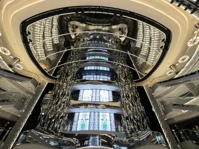 Luxuriöses, mehrstöckiges Atrium der MSC Seaside. Glänzende Spiegelwände, vertikale Lichtstreifen und farbige Buntglasfenster dominieren den hohen Raum.