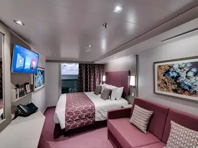 Moderne Balkonkabine an Bord der MSC Seaside mit Doppelbett, Sofa, TV und Balkon mit Meerblick. Das Interieur ist in Lila- und Weisstönen gehalten.