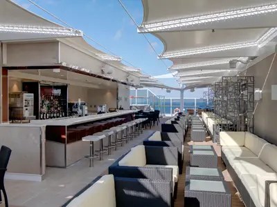 Die Aurea Bar an Bord der MSC Seaside. Ein eleganter, überdachter Barbereich im Freien mit langem Tresen, Barhockern und bequemen Lounge-Sitzgruppen. Der weite Blick reicht bis zum Meer.