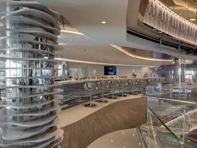 Die elegante Champagne Bar an Bord der MSC Seaside besticht durch eine lange Theke mit Hockern und Champagnerflaschen. Eine skulpturale Chromsäule und moderne Beleuchtung prägen den modernen Raum.