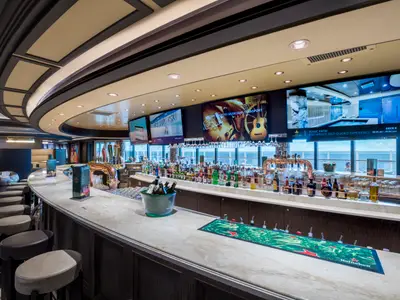 Die moderne Sports Bar an Bord der MSC Seaside. Eine lange Marmortheke mit Barhockern, Bierhähnen, Spirituosen und grossen Bildschirmen. Grosse Fenster bieten Meerblick.