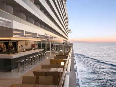 Die Außenterrasse einer Bar an Bord der MSC Seaside mit Barhockern und Tischen. Im Hintergrund ist das offene Meer und der Sonnenuntergang zu sehen.