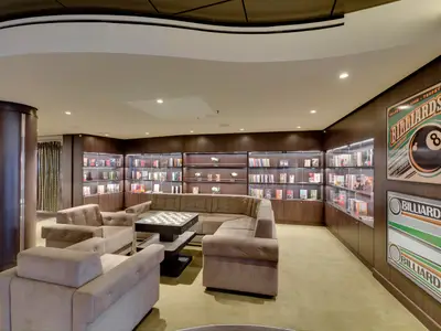 Bequeme Bibliothek-Lounge an Bord der MSC Seaside. Sie bietet Sofas, Sessel, beleuchtete Bücherregale und Billard-Poster an den Holzwänden.