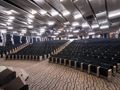 Ein weitläufiges Metropolitan Theater an Bord der MSC Seaside mit dunklen Reihenbestuhlung und einer eleganten Deckenbeleuchtung. Die Bühne ist im Vordergrund links sichtbar.