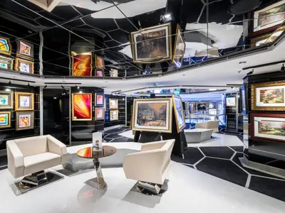 Die stilvolle Kunstgalerie an Bord der MSC Seaside zeigt zahlreiche Gemälde in goldenen Rahmen und modernen Sitzecken. Die Decke ist spiegelnd und schwarz mit weissen Mustern.