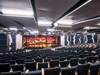 Das Metropolitan Theater an Bord der MSC Seaside. Eine leere Bühne mit großen LED-Bildschirmen, die goldene Masken zeigen, umgeben von dunklen Sitzreihen in einem modernen Saal.