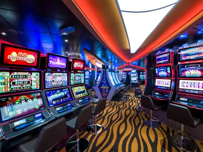 Das Casino an Bord der MSC Seaside zeigt Reihen beleuchteter Spielautomaten und Barhocker. Moderne Deckenbeleuchtung in Rot und Blau prägt die lebhafte Szene.