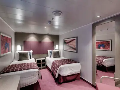 Moderne Innenkabine an Bord der MSC Seaside mit zwei Einzelbetten, dunkelroten Tagesdecken und passendem Teppich. Wandkunst und ein großer Spiegel ergänzen die helle Einrichtung.