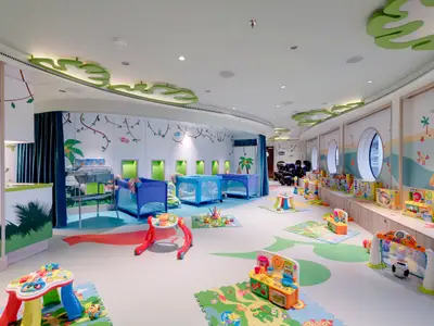 Heller Baby Club an Bord der MSC Seaside mit blauen Babybetten, Wickeltisch und bunten Spielsachen. Dschungel- und Strandmotive schmücken Wände und Bullaugenfenster.