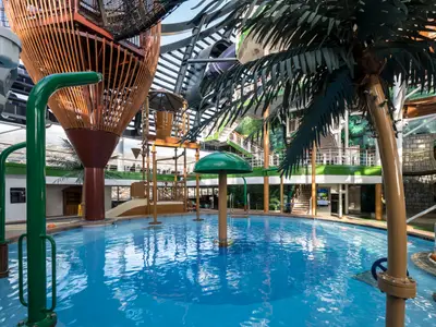 Panoramablick auf den mehrstufigen Forest Aquaventure Park mit Pool, Rutschen und Wasserattraktionen an Bord der MSC Seaside. Tropische Deko, blaues Wasser, und ein Tageslichtdach sind sichtbar.