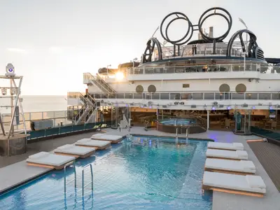 Der offene Poolbereich mit Sonnenliegen und Whirlpool an Bord der MSC Seaside. Im Hintergrund ist das Meer bei Sonnenuntergang zu sehen. Die obere Decks sind sichtbar.