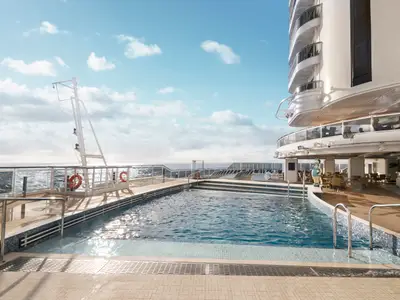 Das South Beach Pooldeck der MSC Seaside. Großes Schwimmbecken, Holzdeck, Sonnenliegen und Meer. Weiße Schiffsarchitektur.