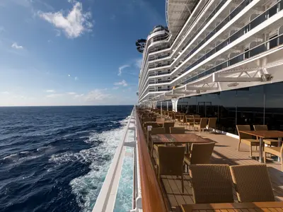 Seitlicher Blick auf die MSC Seaside und das weite Meer bei Tageslicht. Ein Aussenrestaurant mit dunklen Glasfassaden und vielen leeren Tischen ist sichtbar.