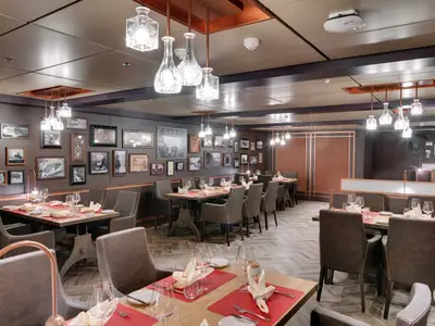 Das Spezialitätenrestaurant Butcher's Cut an Bord der MSC Seaside. Dunkle Wände mit Kunstwerken, Tische mit braunen Stühlen und roten Tischsets. Moderne Hängelampen leuchten den Raum aus.
