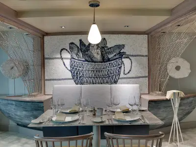 Ein elegantes Spezialitätenrestaurant an Bord der MSC Seaside. Der Raum zeigt einen gedeckten Tisch für vier Personen und eine einzigartige Wand-Mosaik-Kunst.