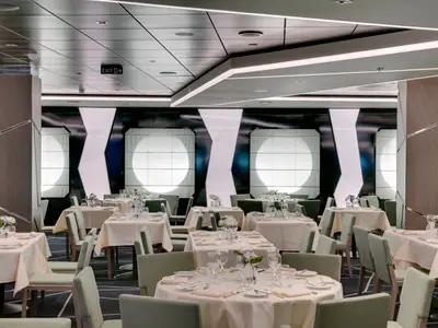 Das modern gestaltete Ipanema Restaurant an Bord der MSC Seaside. Festlich gedeckte Tische mit hellgrünen Stühlen. Stilvolle Wand- und Deckenbeleuchtung. Keine Personen.