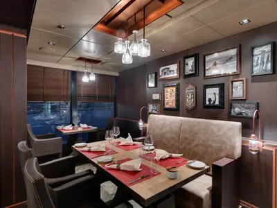 Innenansicht vom Butcher's Cut Steakhouse an Bord der MSC Seaside. Elegante Tische, Ledersessel, Holzwände mit Bildern. Nachtsicht auf beleuchtete Stadt.