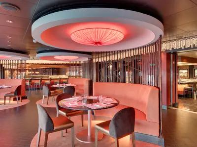 Ein stilvolles asiatisches Spezialitätenrestaurant an Bord der MSC Seaside mit runden roten Deckenleuchten, Holzelementen und eleganten Sitzbereichen.