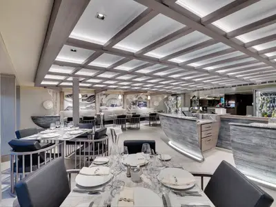 Blick in das elegant gedeckte Spezialitätenrestaurant Ocean Cay an Bord der MSC Seaside. Maritim gestalteter Raum mit Fisch-Mosaiken, Holzbalkendecke, Bar und Weinkühlern.