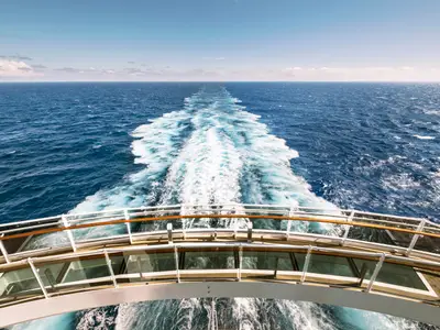 Panoramablick vom Heck der MSC Seaside auf das offene Meer mit der weissen Bugwelle und blauem Himmel. Die Reling der Bridge of Sighs ist unten sichtbar.