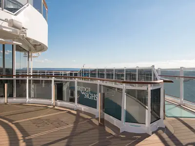 Sonniger Tag auf der MSC Seaside: Glasbrücke Bridge of Sighs ragt über das Meer, umrahmt von hölzernen Decks und modernen Glasgeländern. Heller Himmel und weite Ozeansicht.