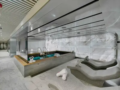Der luxuriöse Spa-Bereich "MSC AUREA SPA" an Bord der MSC Seaside. Ein Pool, ergonomische Liegen und hinterleuchtete Marmorwände sind sichtbar. Weiße Handtücher liegen bereit.