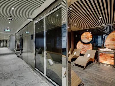 Salz-Ruheraum im MSC Aurea Spa an Bord der MSC Seaside mit Liegen, beleuchteten Salzsteinwänden und Kiste. Heller Gang durch Glas sichtbar.