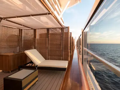Überdachter Aussenbereich des MSC Aurea Spa an Bord der MSC Seaside. Eine Lounge-Liege und Beistelltisch in einer privaten Bambus-Kabine. Rechts offener Meerblick bei Sonnenuntergang.