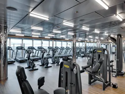 Ein modernes Fitnessstudio an Bord der MSC Seaside, ausgestattet mit Technogym-Tretmühlen, Fahrrädern und Kraftgeräten. Große Fenster bieten einen weiten Blick auf das Meer.