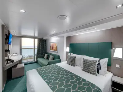 Geräumige Balkonkabine der MSC Seaview mit grossem Doppelbett, grüner Tagesdecke, Sofa und Schreibtisch. Der Balkon bietet Meerblick.