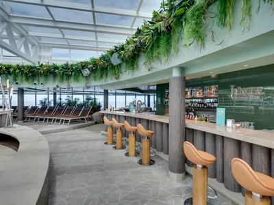 Die tropische Jungle Beach Bar an Bord der MSC Seaview. Pflanzenreiche Decke, Holztheke, orangefarbene Barhocker und Fenster mit Meerblick. Liegestühle im Hintergrund.