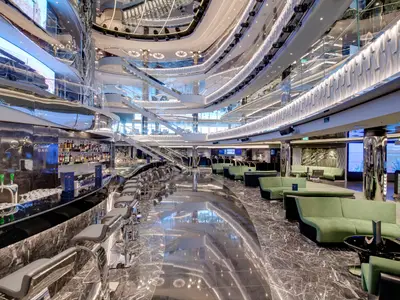 Blick in die elegante, mehrstöckige Seaview Bar und Lounge im Atrium an Bord der MSC Seaview mit geschwungener Bar, grünen Sofas und glänzenden Oberflächen.