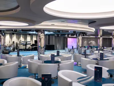 Elegante Haven Lounge an Bord der MSC Seaview. Moderne weiße Sessel, runde Tische, eine Bühne mit Instrumenten und eine große LED-Wand.