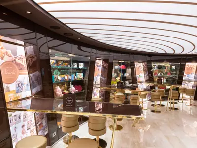 Die Venchi 1878 Chocolate Bar an Bord der MSC Seaview zeigt eine moderne Bar mit goldenen Theken und Hockern sowie Vitrinen mit Schokoladenprodukten und italienischen Motiven.