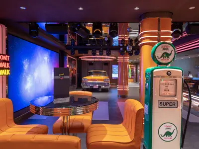 Der farbenfrohe Garage Club an Bord der MSC Seaview mit einem orangefarbenen Oldtimer, einer Vintage-Tankstelle und neonbeleuchteten Sitzbereichen.