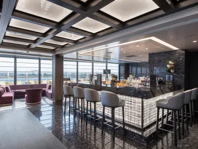 Die stilvolle Seaside Lounge an Bord der MSC Seaview. Beleuchtete Bar mit Hockern und bequeme lila Sitzbereiche befinden sich vor großen Panoramafenstern mit Meerblick auf einen Hafen.
