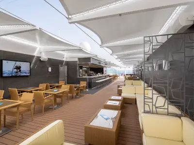 Die Aurea Bar an Bord der MSC Seaview mit dunklen Wandfliesen, heller Bestuhlung und Barhockern. Überdacht mit weissen Sonnensegeln, offener Bereich zum Meer. Die Einrichtung ist modern und einladend.