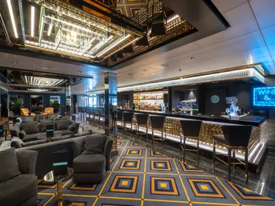 Eine elegante Bar-Lounge an Bord der MSC Seaview mit dunklen Sofas, goldenen Akzenten und einer langen Bar, die von einem blauen Neonlichtschild "WINE & COCKTAILS" beleuchtet wird. Die Decke ist verspiegelt, und der Teppich hat ein geometrisches Muster in Blau und Gold.