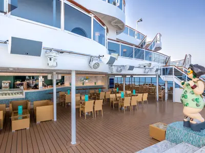 Blick auf die Panorama Bar und Lounge an Bord der MSC Seaview mit leeren Tischen, Stühlen und einer bunten Skulptur auf dem Holzdeck. Im Hintergrund ist das Meer zu sehen.