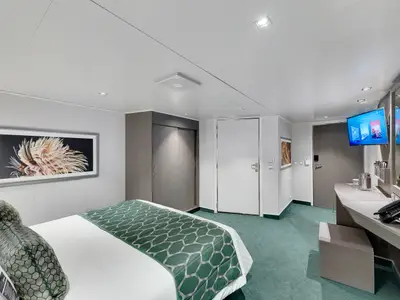 Eine geräumige, barrierefreie Innenkabine an Bord der MSC Seaview. Sie zeigt ein komfortables Doppelbett mit grüner Bettwäsche, einen Schreibtischbereich mit Spiegel und TV sowie einen großen Kleiderschrank.