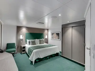 Helle, barrierefreie Innenkabine an Bord der MSC Seaview. Doppelbett, grüne Bettdecke und Teppich. Moderner Schreibtisch, Sessel und Schiebetüren-Kleiderschrank.