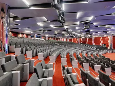 Panoramablick auf das geräumige Odeon Theater an Bord der MSC Seaview. Reihen von grauen und weißen Sitzen sind auf einem roten Teppichboden angeordnet, umgeben von modernen, rot-weißen Wandpaneelen und einer stilvollen Decke mit Beleuchtung und Bühnentechnik.