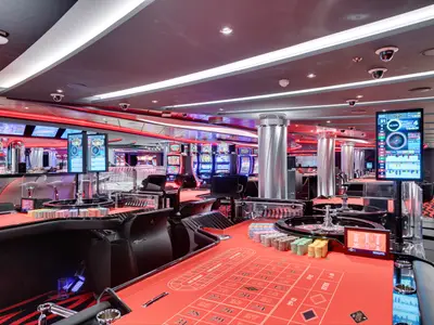 Ansicht des Platinum Casinos an Bord der MSC Seaview. Rote Roulettetische mit Jetons und Bildschirmen im Vordergrund. Dahinter beleuchtete Spielautomaten und eine Bar. Elegantes Design mit roten Lichtakzenten. Ohne Personen.