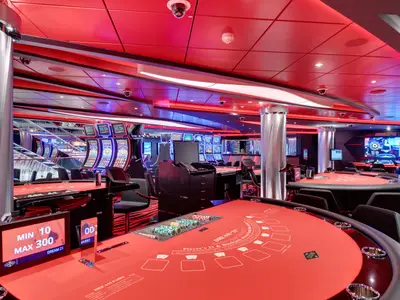 Ein modernes, rotes Casino an Bord der MSC Seaview mit glänzenden Spielautomaten, leeren Blackjack-Tischen und einem Roulette-Tisch im Hintergrund, beleuchtet von roten und blauen LEDs.