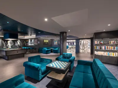 Moderne Lounge an Bord der MSC Seaview mit Billardtisch, Schachbrettern und Bibliothek. Teal-Sofas, dunkle Wände, Art-déco-Bilder und beleuchtete Bücherregale laden zum Verweilen ein.