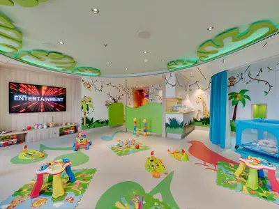 Heller Baby Club Chicco an Bord der MSC Seaview. Dschungel-Wandmalereien, bunte Spielsachen, TV und blaues Babybett. Ein Wickelbereich ist ebenfalls vorhanden.