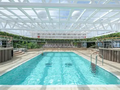 Jungle Pool an Bord der MSC Seaview, überdacht mit Glasdach. Türkisblaues Wasser, umgeben von Pflanzen und Sonnenliegen. Helles Tageslicht. Ohne Personen.