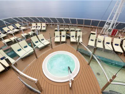 Blick von oben auf den luxuriösen Poolbereich des MSC Yacht Clubs an Bord der MSC Seaview mit einem runden Whirlpool und vielen Sonnenliegen auf dem Deck. Im Hintergrund ist das Meer zu sehen.